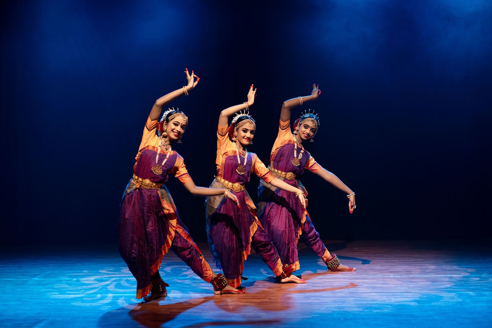 Three dancers performing under blue stage lighting
