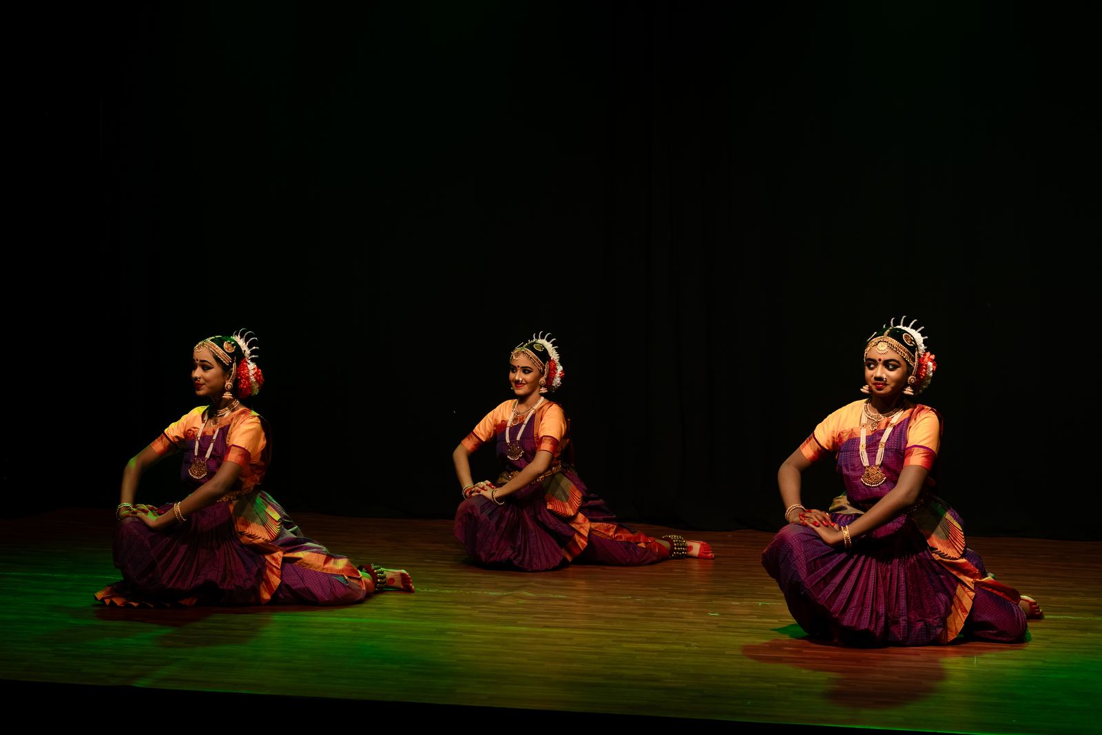 Three Bharathanatyam dancers seated in a stage formation
